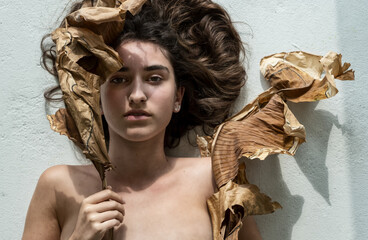 Portrait of a young sexy woman with brown hair artfully decorated between leaves of dry, withered banana tree looking like an art nouveau girl, copy space.
