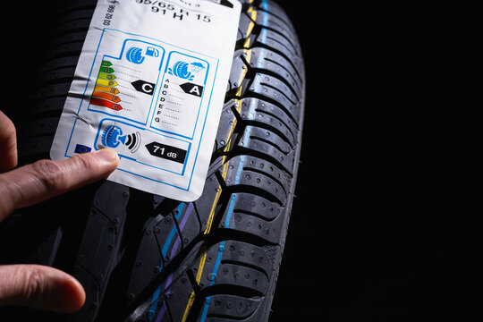 Label on tire with information about level of noise, braking distance on wet road, fuel efficiency. Finger shows on information sticker on tire.