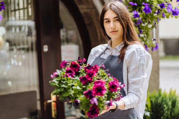 Mixed race woman worker or store owner with standing in the doorway of her grocery shop looking aside smiling. Portrait of girl assistant wearing apron welcoming inviting open door of store.