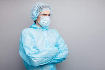 Photo of guy doc virology center clinic arms crossed came to see covid patient look empty space wear face mask hazmat blue uniform suit plastic facial goggles isolated grey color background