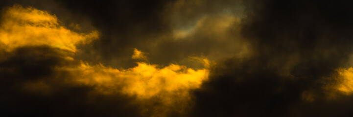 Panorama fluffy storm clouds illuminated by disappearing rays at sunset and dark thunderclouds floating across sky to change season weather. Soft focus, motion blur sky landscape.