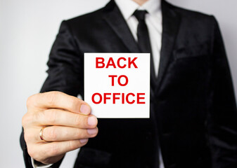 The phrase Back to office on a white piece of paper held by a young man in a business suit.