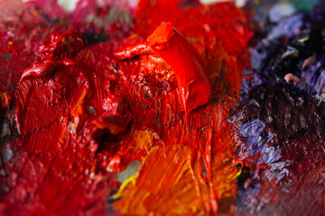 Red oil paint on the artist's palette. Hobbies and leisure: mixing paints. Top view of the palette. Shades of red paint. Cadmium red and madder lake red.Creative process. Selective focus.