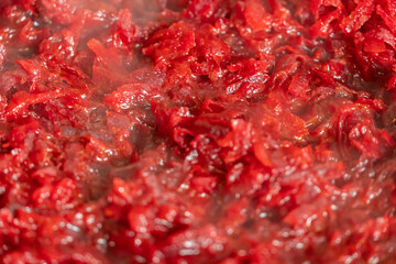 Raw grated beets stewed in a pan, steam, background