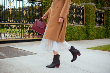 Detail of young fashionable woman wearing beige wool coat, tulle midi skirt and black high heel...