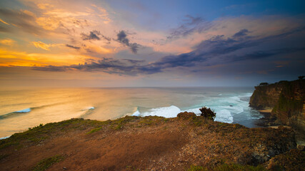 Seascape. Spectacular view from Uluwatu cliff in Bali. Sunset time. Blue hour. Ocean with motion foam waves. Cloudy sky. Nature concept. Soft focus. Slow shutter speed.