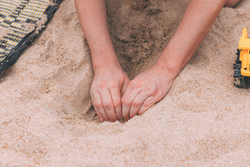 Father's day. Man's hands digging a hole in the sand to build a deep tunnel. Games in the sand with a child. Toy cars. Entertainment for children and adults. It's more fun together. Two hands
