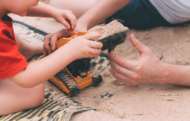 Father's day. Dad and son. Little son plays toys with dad on the beach with sand. Happy loving family. Happy family father and child. Toy cars. Hands of a man and a small child on the beach. Together