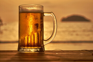 A big glass of draft beer during sunset with a sea at the background