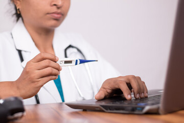 Doctor explaining how to use fever thermometer to patient through online on laptop - Concept of telehealth, or telemedicine with patient during coronavirus or covid-19 pandemic.