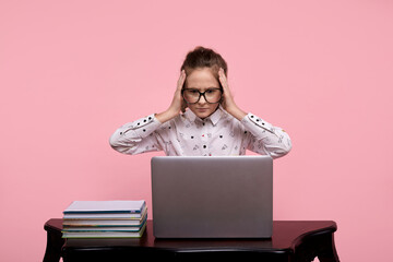 A surprised young girl sits at a laptop in white shirt and black-rimmed glasses