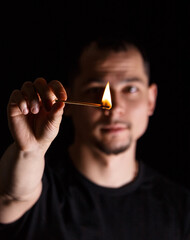 Man holding burning match stick in front of blurred face on dark background