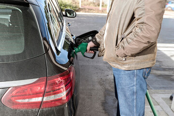 A man holds a nozzle supplying unleaded petol while he refuels a car at a petrol station - UK - obrazy, fototapety, plakaty