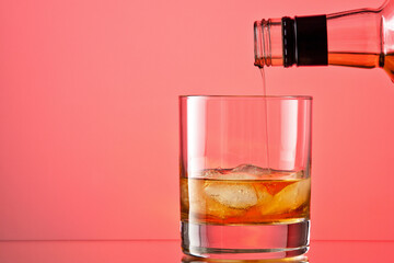 bottle (alcohol drink) filling a glass, with ice, on a pink background