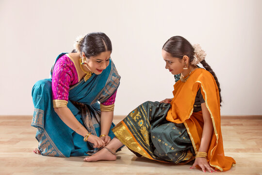 Bharatnatyam dancer tying an anklet on her student&rsquo;s feet. 
