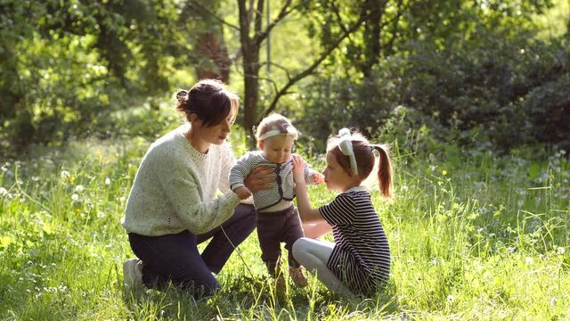 Mother with elder sister daughter and toddler baby child happy family play togather on city park spring green nature