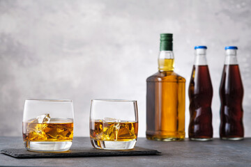 Glass with whiskey and ice cubes on background bottle
