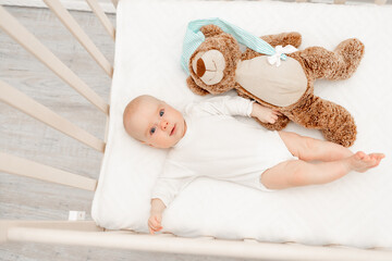 Sleeping baby and his toy in white crib. Nursery interior and bedding for kids. Cute little boy...