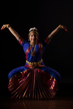 Bharatnatyam dancer in a garuda lingam pose during her performance on a dark background. 
