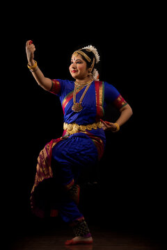Bharatnatyam dancer in a saraswati pose during her performance on a dark background. 
