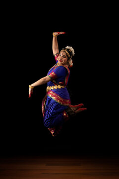 Bharatnatyam dancer jumping in the air in front of a black background. 

