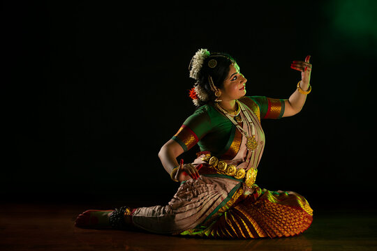 Bharatnatyam dancer playing veena during her performance in front of a dark background. 
