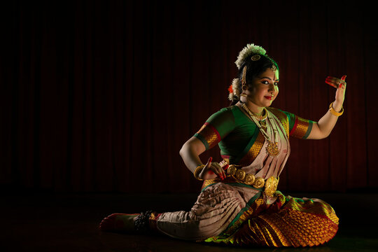 Bharatnatyam dancer playing veena during her performance in front of a dark background. 

