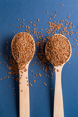 Two wooden spoons with brown Flax seeds on blue background, flat lay.