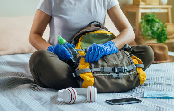 Close Up Of Young Woman Packing Her Backpack With Hand Sanitizer. Prepairing For A Travel After The End Of Quarantine. New Life After Pandemic COVID-19 Concept.