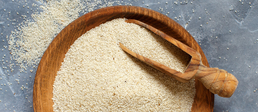 Raw uncooked fonio seeds with a spoon grey background