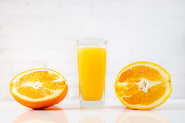 Freshly squeezed orange juice in a glass on a table with slices of oranges next to it. Refreshing yellow beverage with fruits on white background