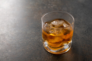 Glass of aged golden whiskey with ice cubes on the table. Amber colored alcohol beverage with rocks at the bar