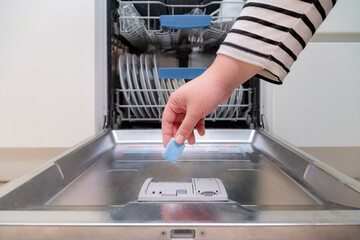 Close up of hand inserting soap capsule into dish washer in the kitchen. Person putting dish...