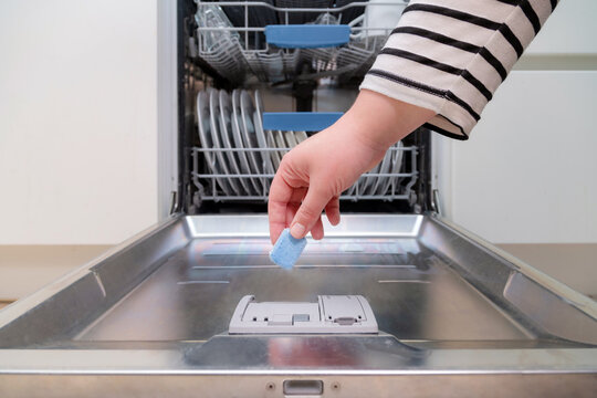 Close Up Of Hand Inserting Soap Capsule Into Dish Washer In The Kitchen. Person Putting Dish Washing Detergent Into Machine