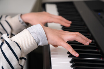 Closeup of teenager playing piano in home music studio. Girl having online class and practicing on modern electric piano