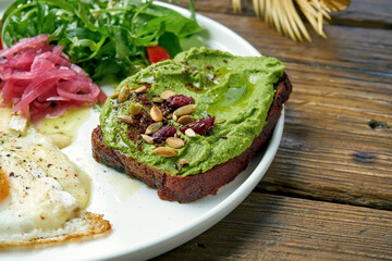 A healthy and balanced breakfast - scrambled eggs with camembert, arugula salad and avocado toast. Wood background