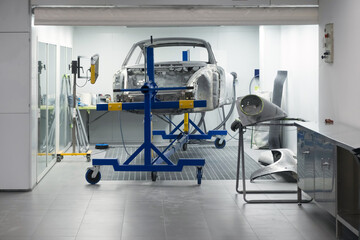 Custom car being build in workshop. Sports car body, car frame is assembled by mechanics. Metallic auto chassis in the air, car skeleton in service
