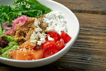 Superfood - a bowl with rice, salmon, guacamole, poached egg and cherry tomatoes seasoned with Greek yogurt on a wooden background. Balanced food