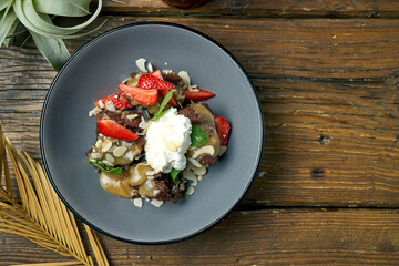 Appetizing brownie dessert cake with ice cream, strawberries and almonds in a gray bowl on a wooden background