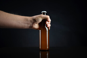 Men holding cold unopened bottle of beer with cap on black background. Hand holding glass of refrigerated wheat or lager beer on dark background