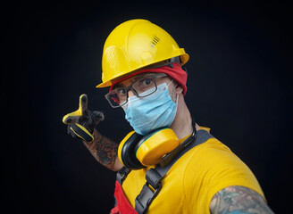 Fototapeta premium a man in a construction repairman's overalls wearing a medical mask against the flu coronavirus and a hard hat on his head