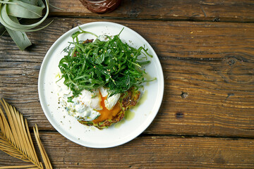 Zucchini pancake with Greek yogurt, arugula and poached egg on a wooden background. Tasty and healthy breakfast