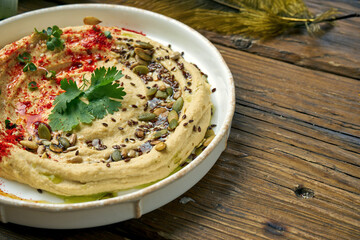Classic oriental appetizer - chickpea hummus in a white plate on a wooden background. Close up