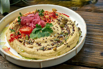 Classic oriental appetizer - chickpea hummus in a white plate on a wooden background. Close up