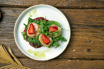 Appetizing toast with goat cheese, red jam, arugula and strawberries with rye bread on a plate on a wooden background