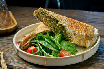 Vegetarian shawarma roll with spinach, tomatoes, hummus and melted cheese in a plate on a wooden background