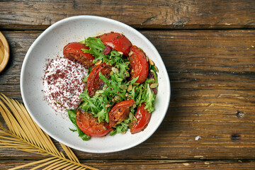 Vegetarian salad with baked tomatoes, greek yogurt and arugula in a bowl on a wooden background