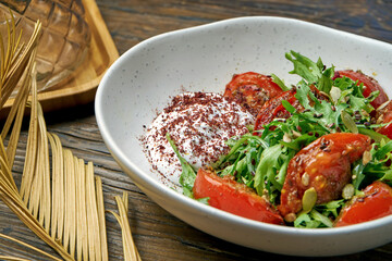 Vegetarian salad with baked tomatoes, greek yogurt and arugula in a bowl on a wooden background