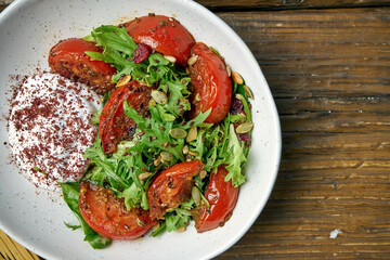Vegetarian salad with baked tomatoes, greek yogurt and arugula in a bowl on a wooden background