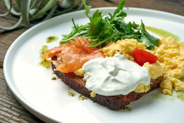 Appetizing breakfast - scramble eggs, with arugula, salmon and toast with Greek yogurt in a plate on a wooden background